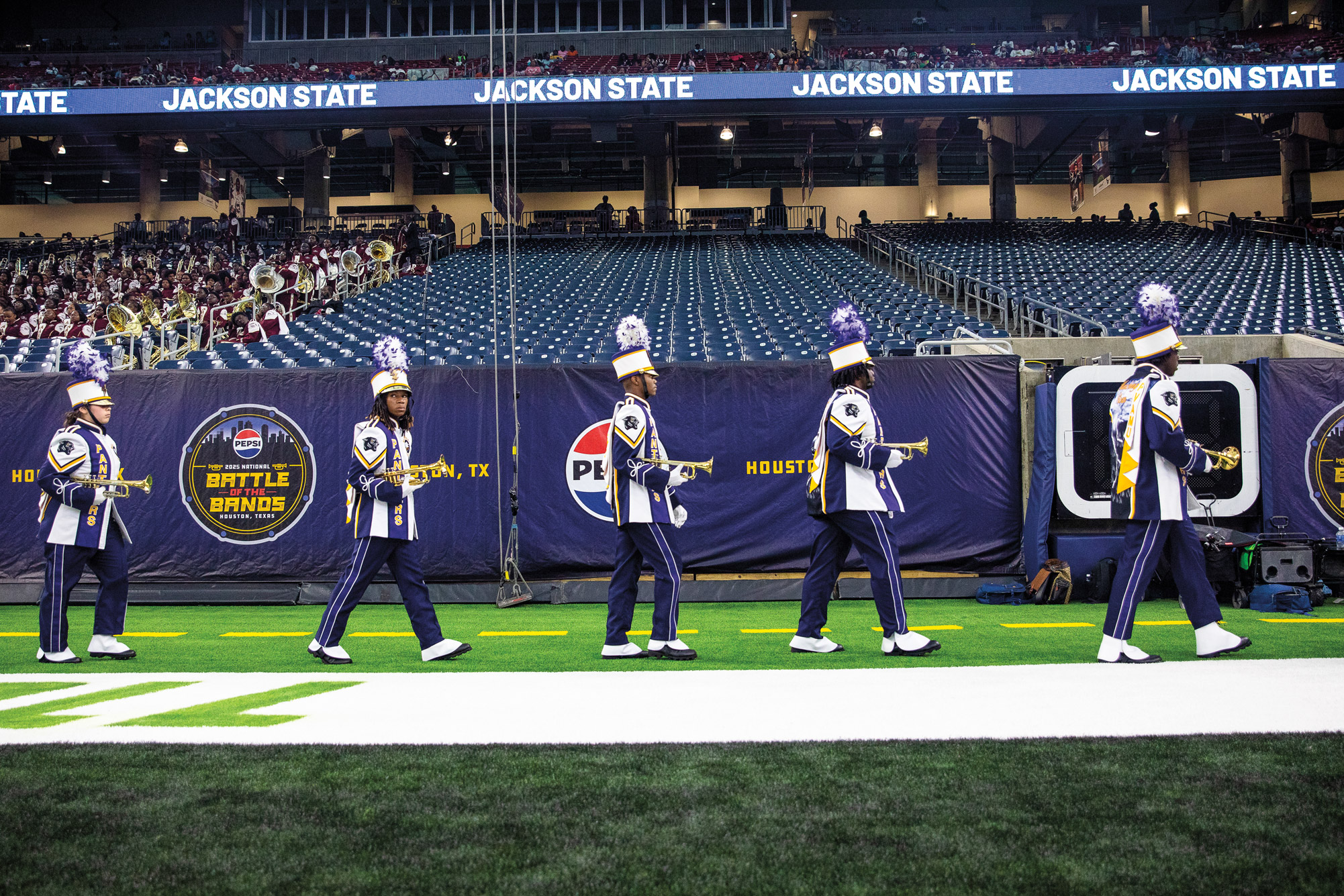 Trumpet players in a marching band walk across the end zone of a football field
