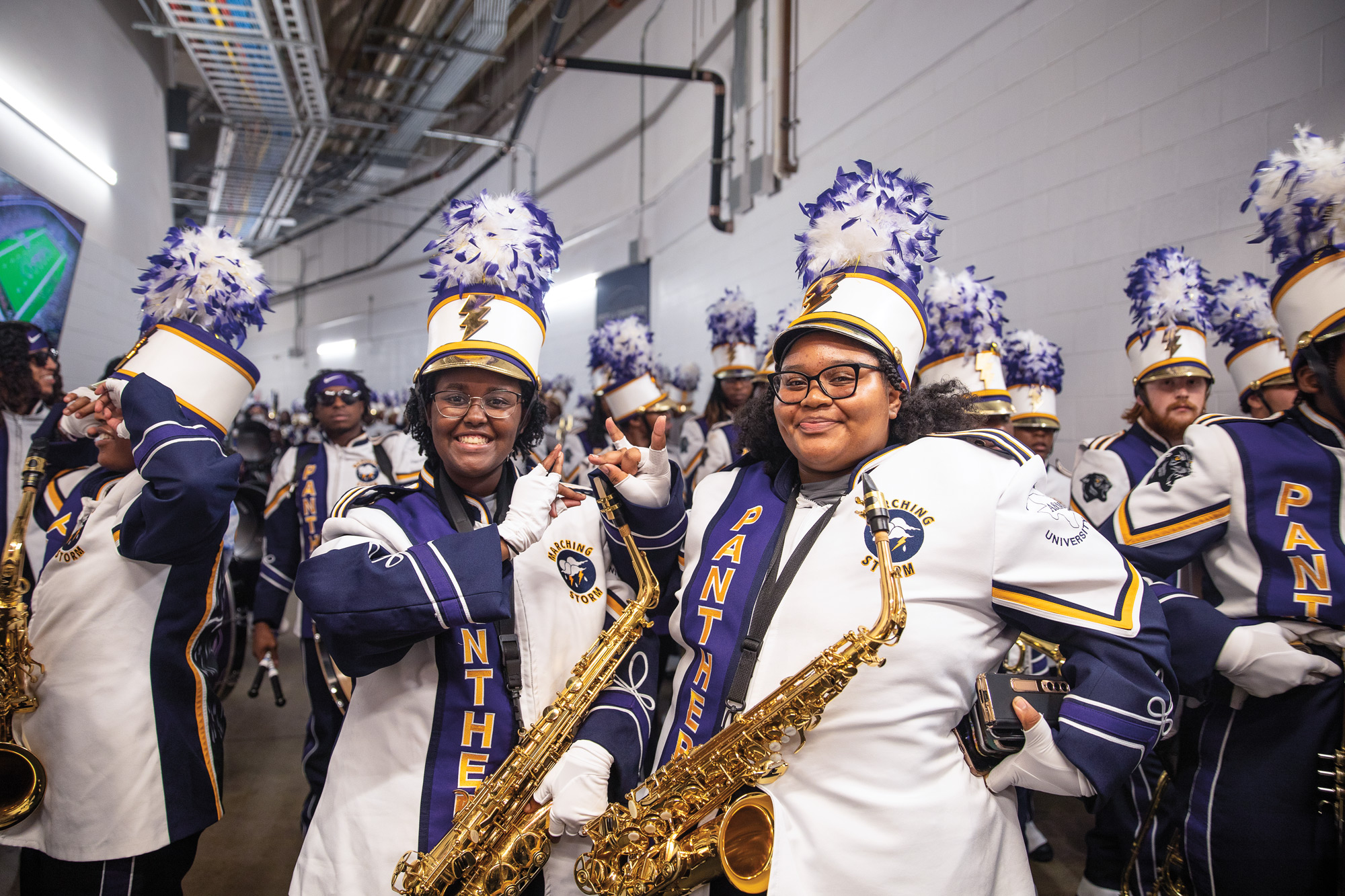 Saxophone players in a marching band smile beneath a large stadium