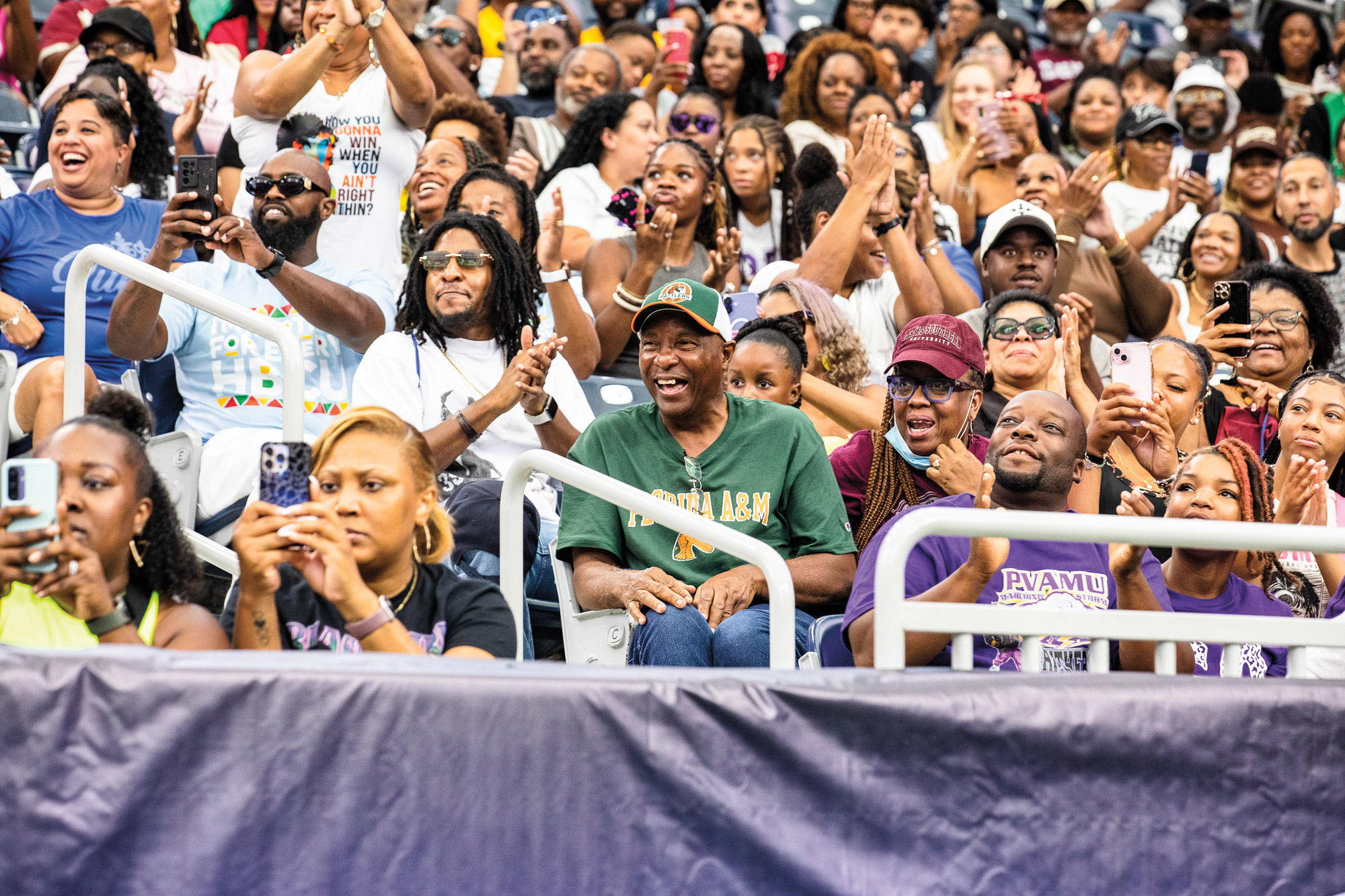 A large group of smiling fans in various colored clothing at a large arena