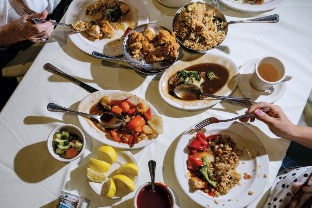 Many plates of food on a white tablecloth, including chicken, rice, broccoli, and more