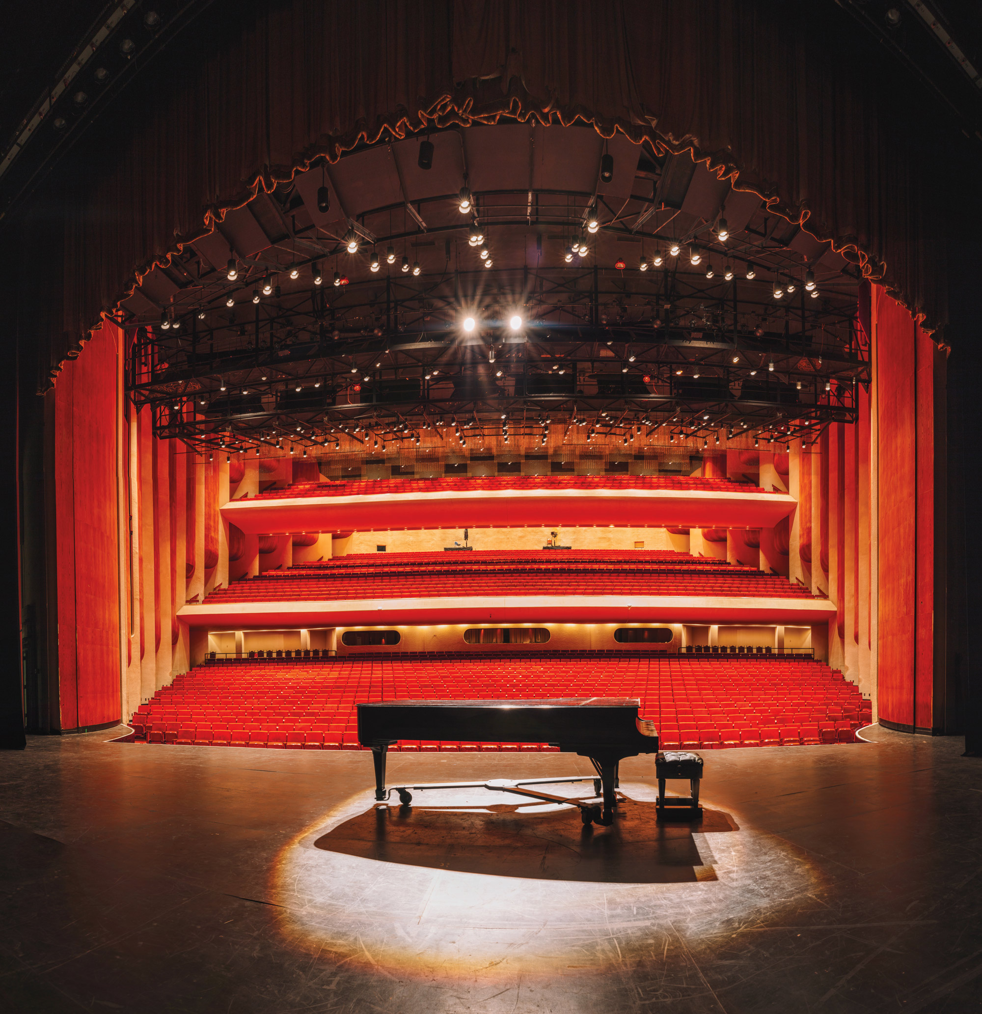A black piano on a lighted stage with empty red seats in a theatre visible