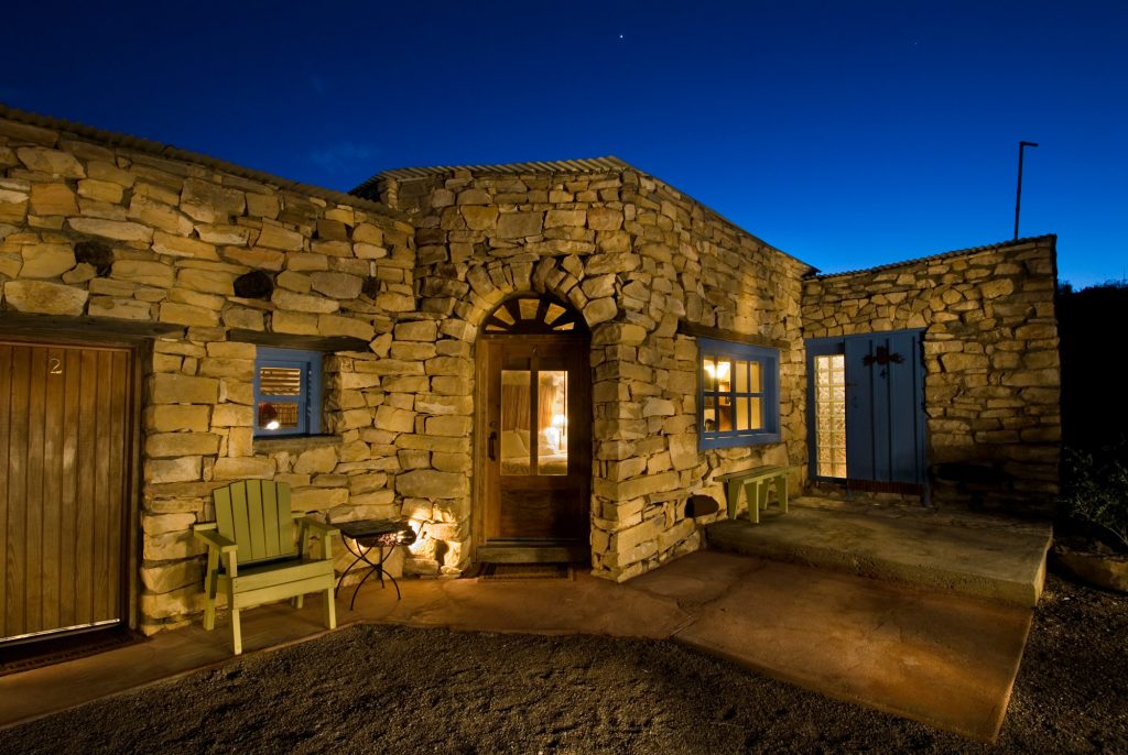 A stone hotel under the night sky with a wooden chair and wooden bench outside