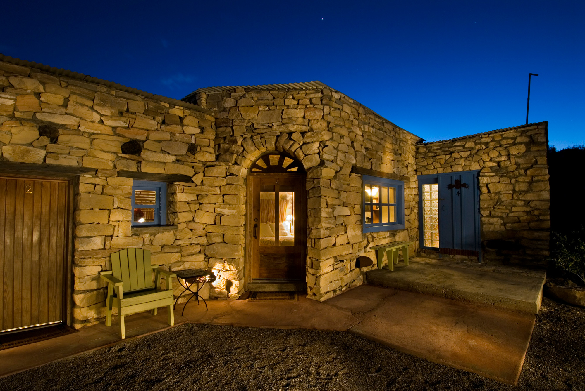 A stone hotel under the night sky with a wooden chair and wooden bench outside