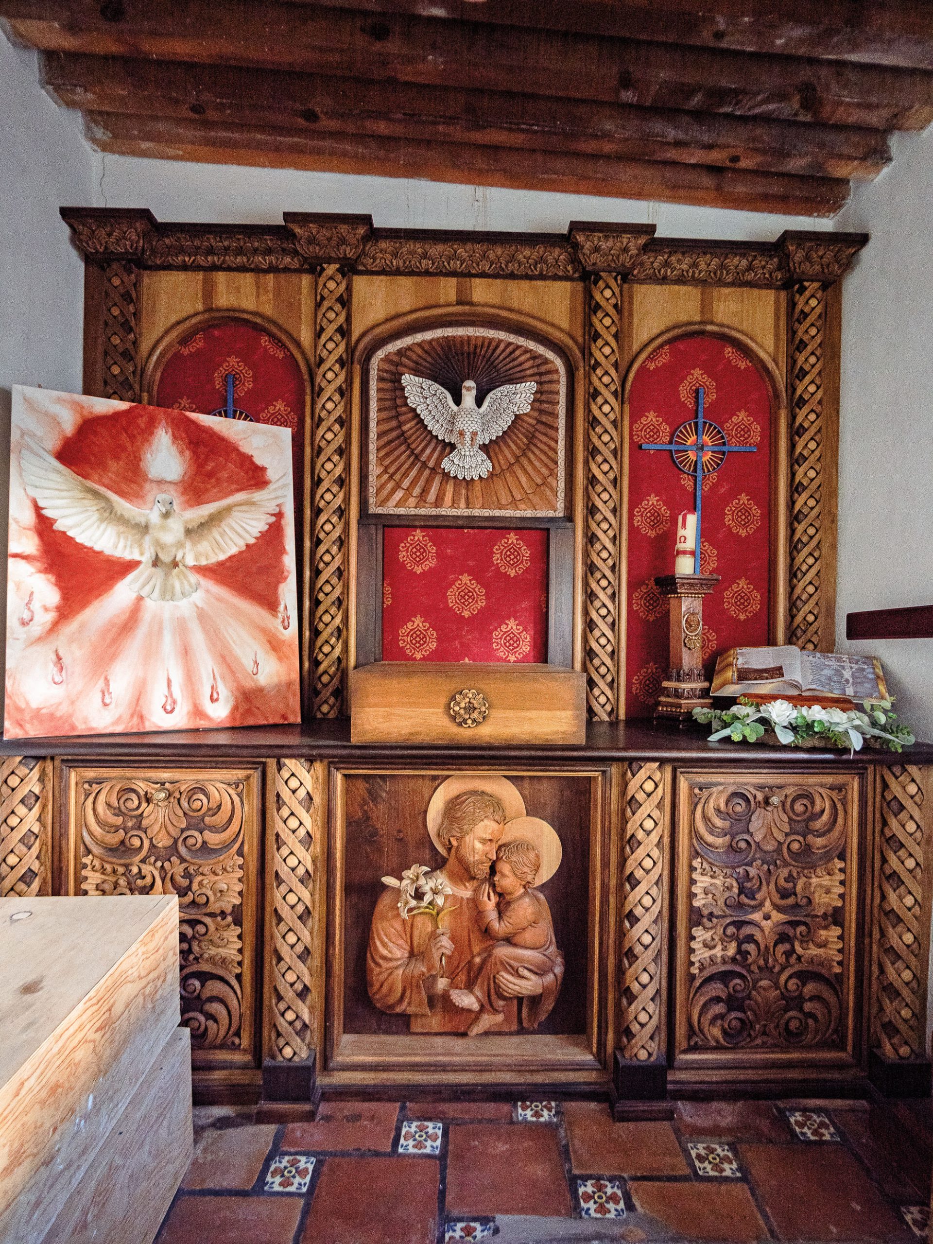 An ornate wooden and red upholstered altar depicts doves, crosses, and Christ.