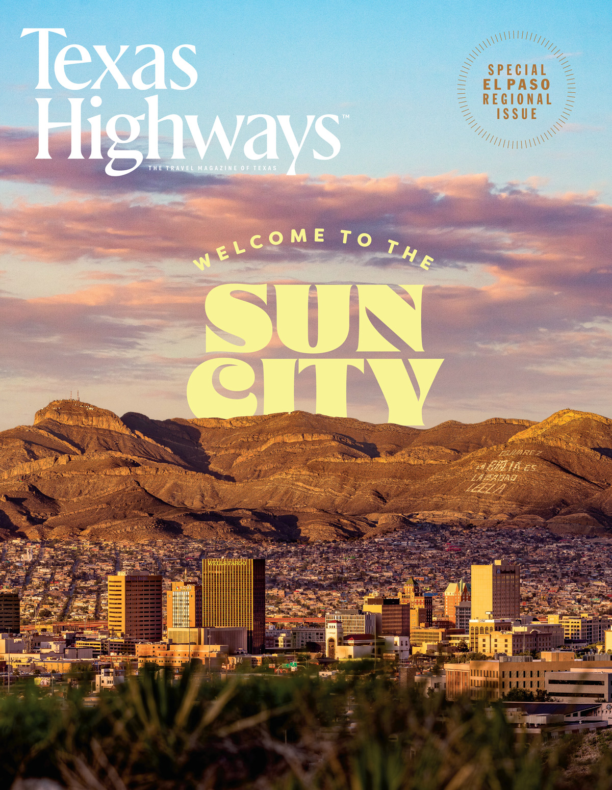A city downtown with large buildings and large brown mountains in the distance at sunset, with the words Welcome to the Sun City visible in yellow text above