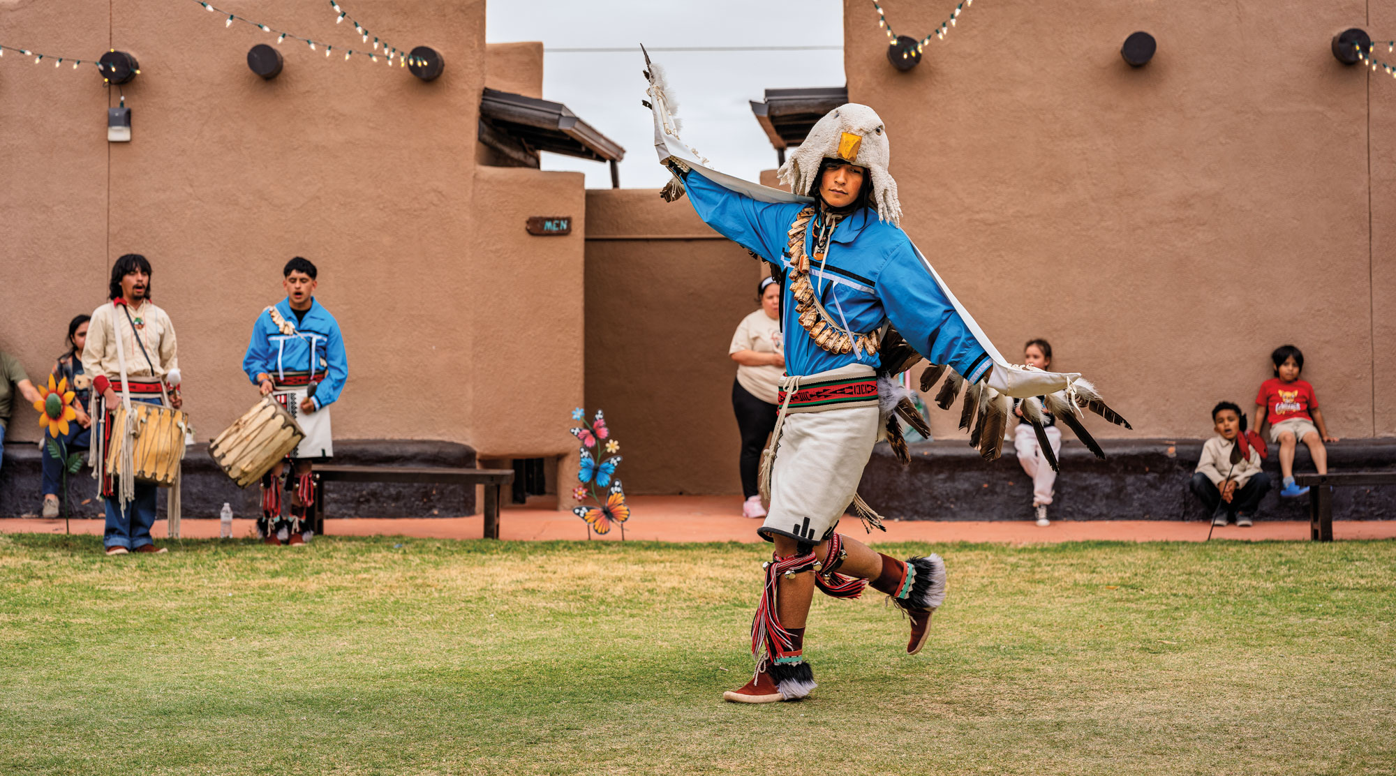 A man wearing a traditional Indigenous eagle headdress dances in a field of grass in front of others.