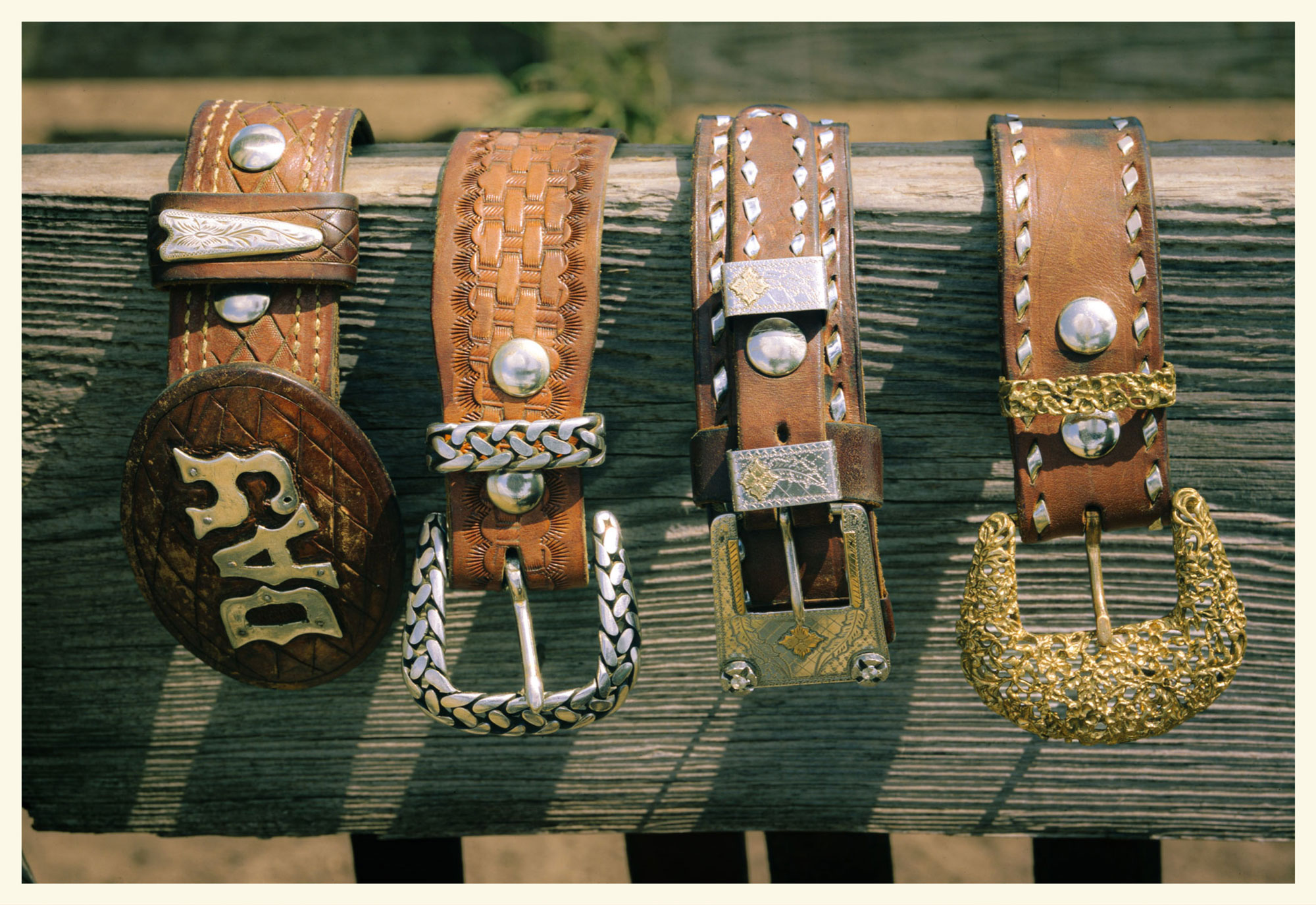 Four vintage belt buckles with brown leather straps resting atop a wooden post