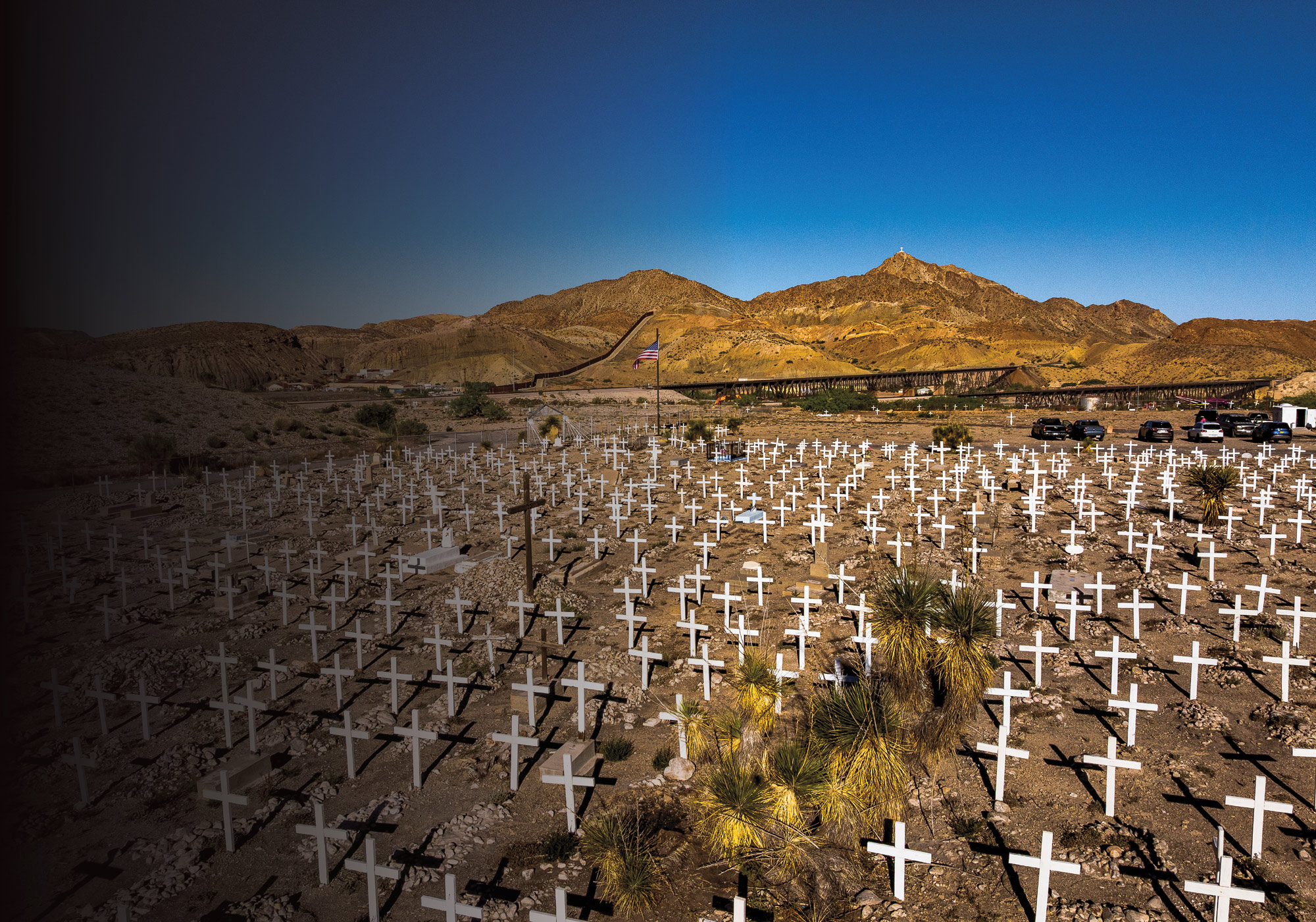 A large cemetery with many white crosses in the ground in front of large mountains