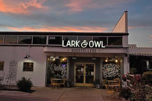 A building with colorful writing on its windows and a sign that reads Lark & Owl Booksellers
