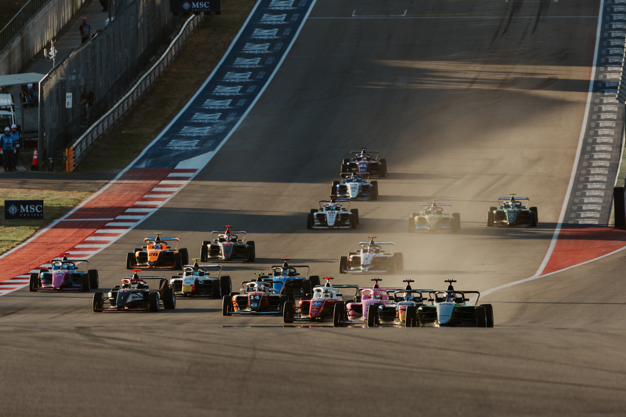 Many Formula 1 race cars descending down a track with smoke on the right side