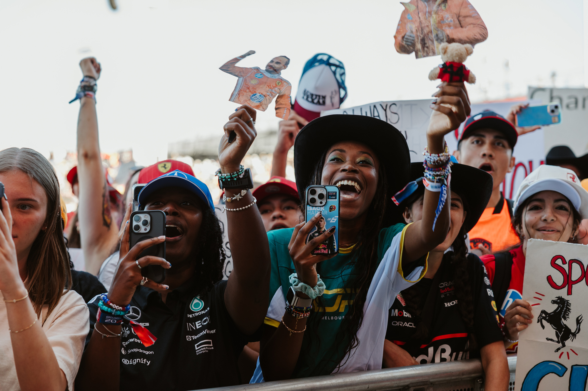 Fans hold up phones and signs depicting Lewis Hamilton near a barricade