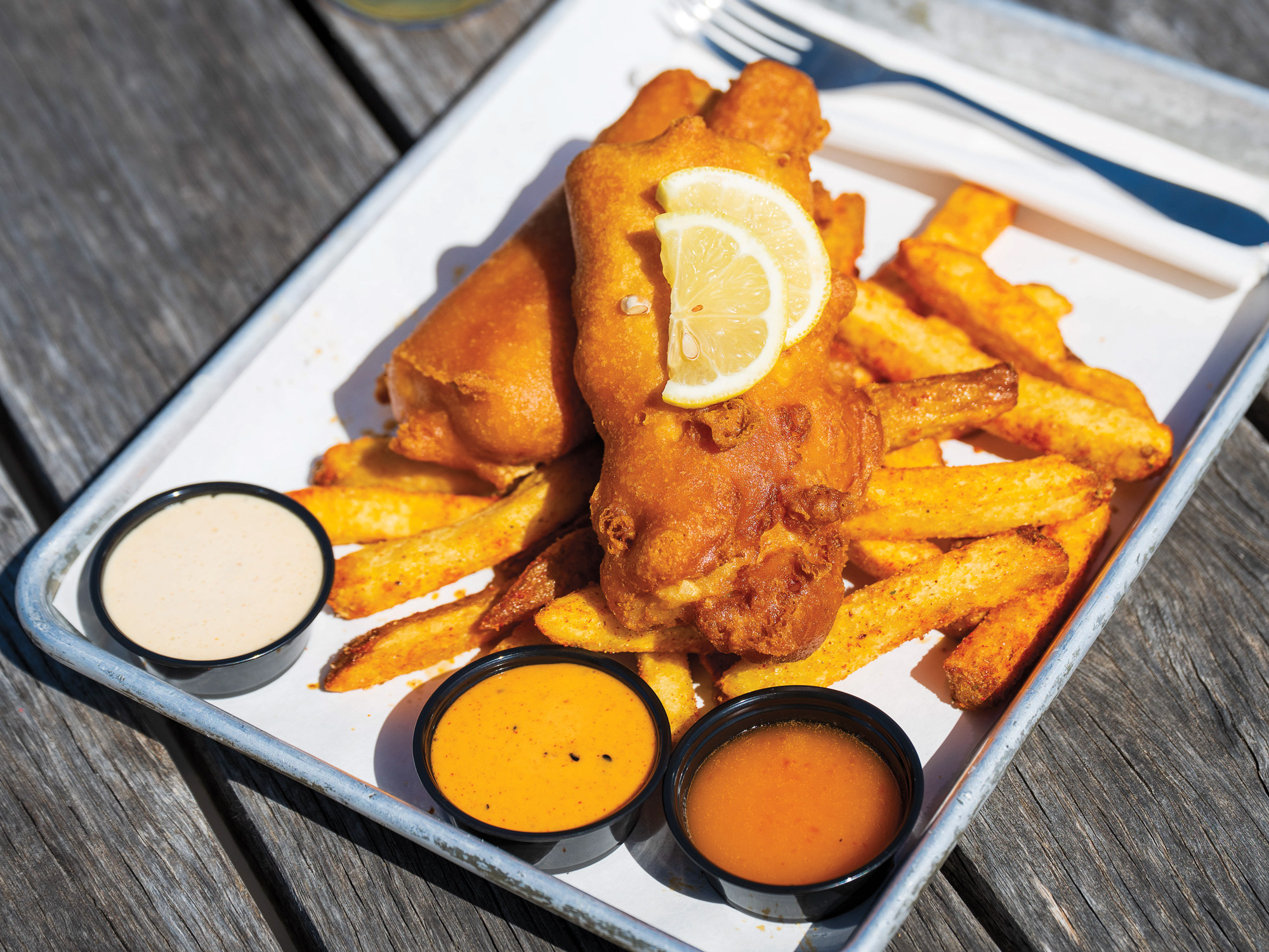 Lemon slices atop fried meat stop French fries with three dipping sauces next to it