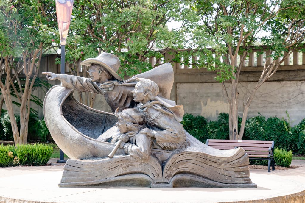A statue of a large book, open in the middle, with three children emerging from it in a canoe