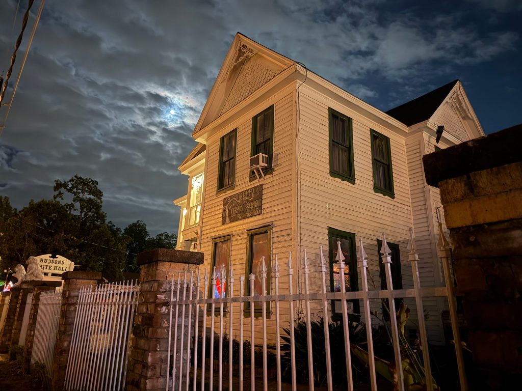 An old white house with a white metal fence in front of it at night