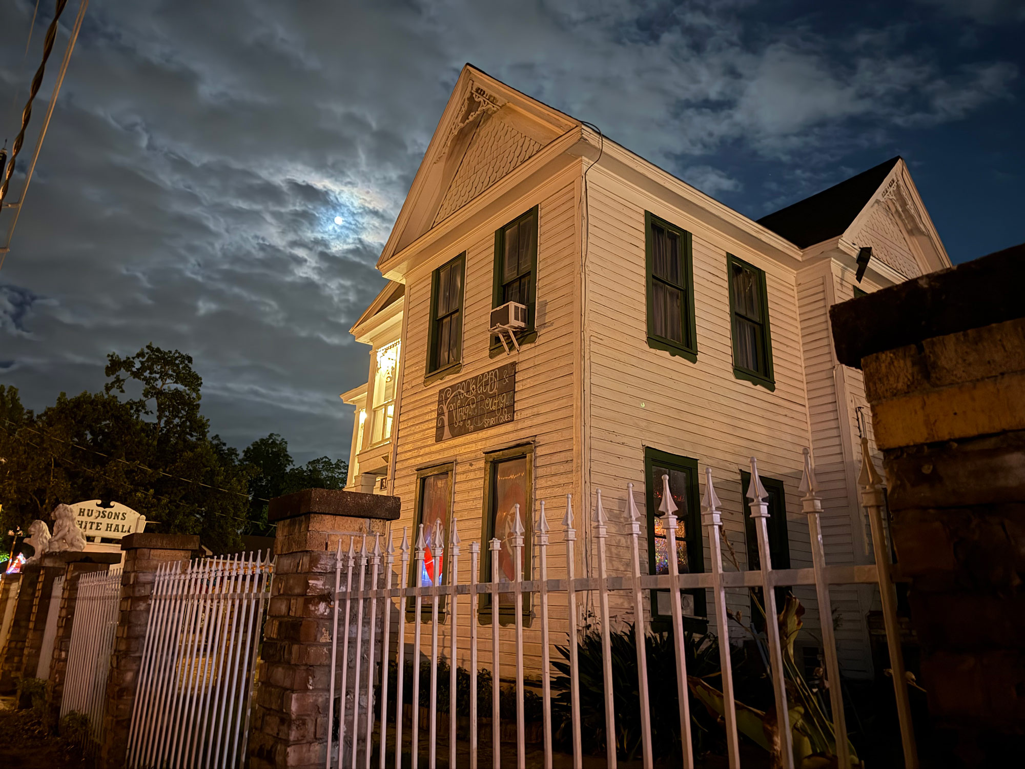 An old white house with a white metal fence in front of it at night